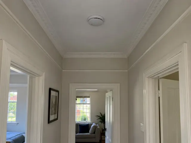 Ceiling smoke alarm in a white hallway with ornate cornices and doorways in Haberfield